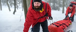 山岳救助隊の救急隊員が、冬季の森林や負傷者を��担架に乗せて屋外で活動します。