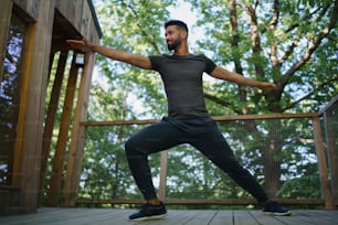 Una vista de ángulo bajo de un joven feliz haciendo ejercicio al aire libre en la terraza de la casa del árbol, fin de semana y concepto de desintoxicación digital.