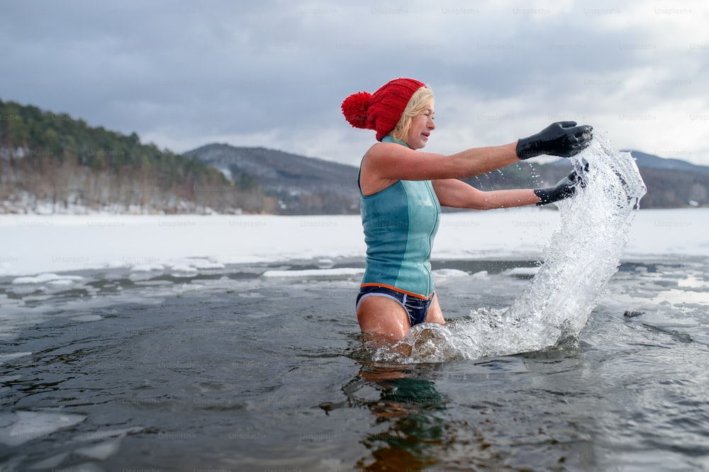 An active senior woman in swimsuit outdoors in winter in frozen lake, cold therapy concept.