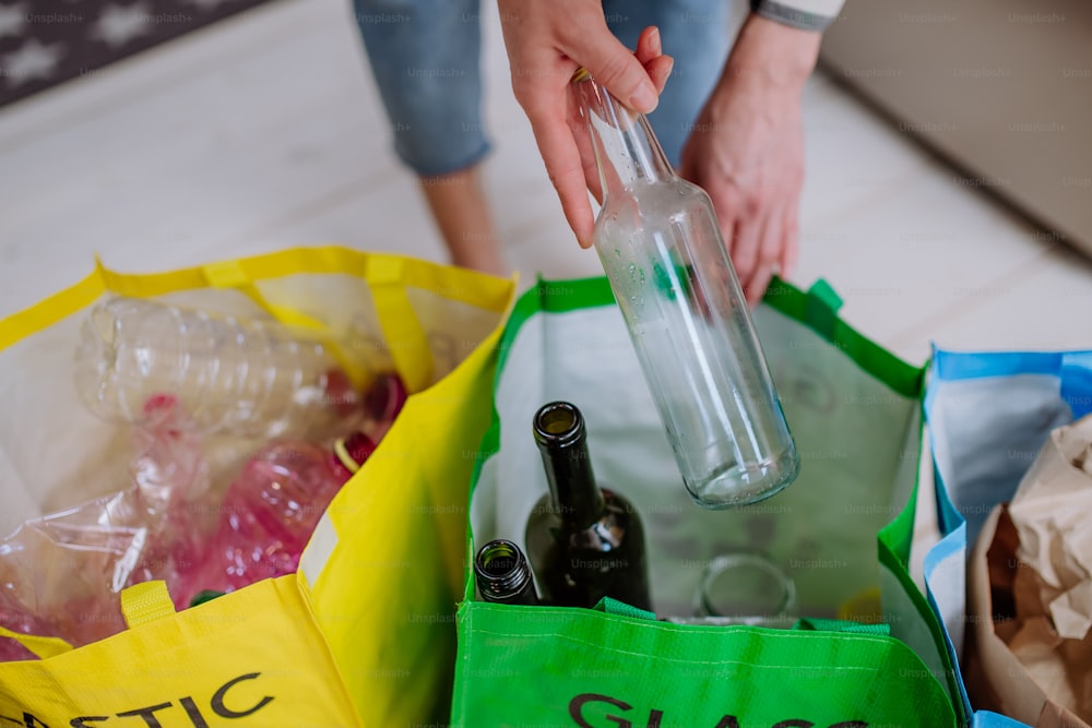 Midsection of a woman throwing empty glass bottle in recycling bin in kitchen.