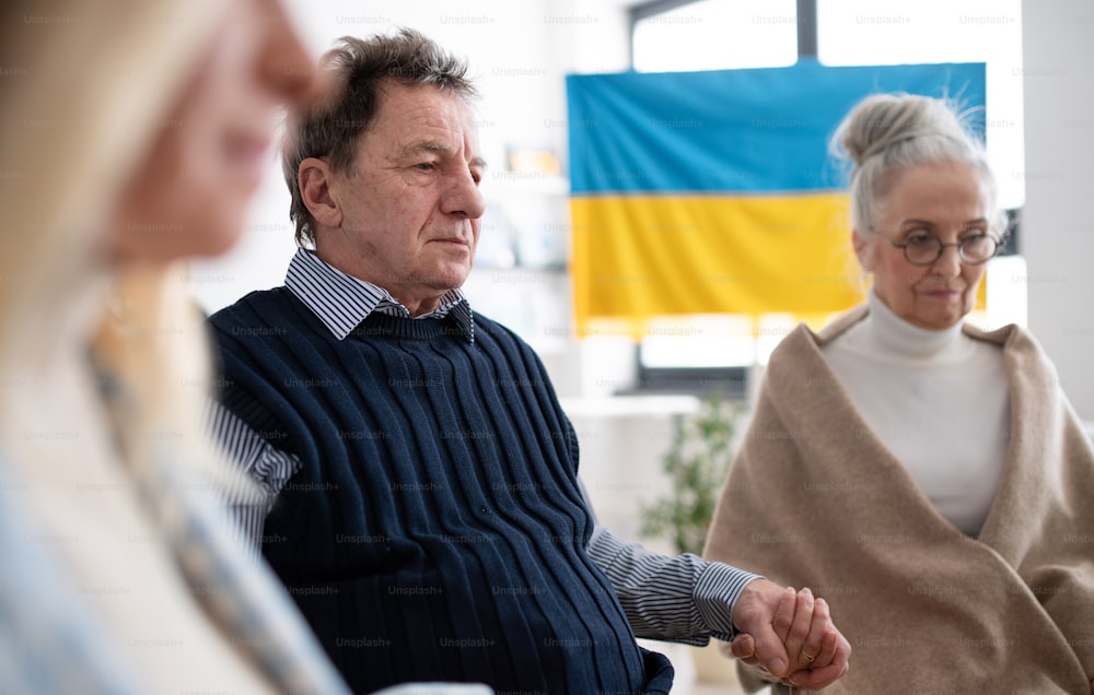 Un grupo de personas mayores tomadas de la mano y orando juntos por Ucrania en el centro comunitario de la iglesia.