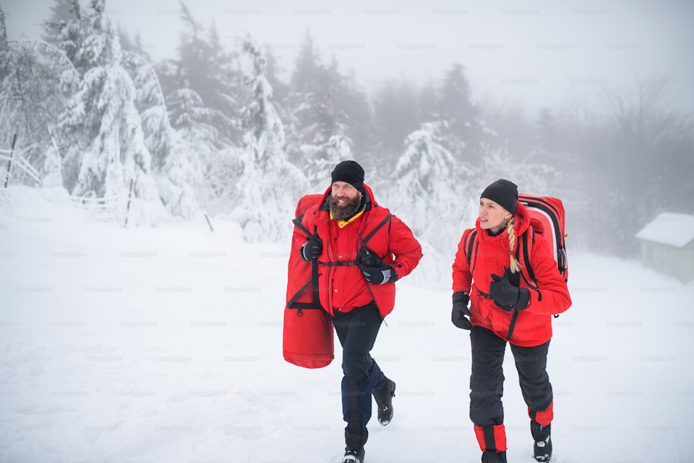 Man and woman paramedics from mountain rescue service running outdoors in winter in forest.