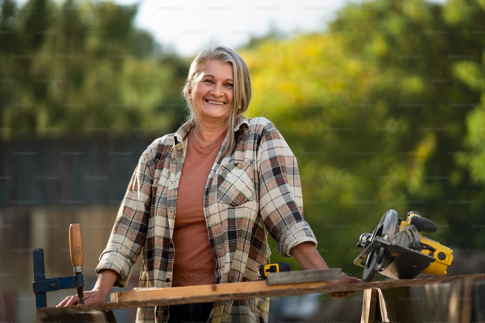 A happy handy female carpenter working in carpentry diy workshop outdoors with circular saw