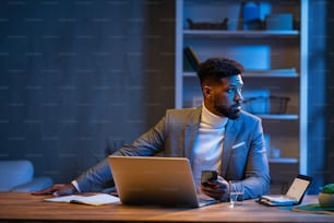 A young african american businessman working indoors in office at night.