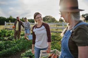 Feliz granjera adulta de mediana edad abrazando a su compañera mayor sosteniendo una canasta con verduras de cosecha propia al aire libre en una granja comunitaria.