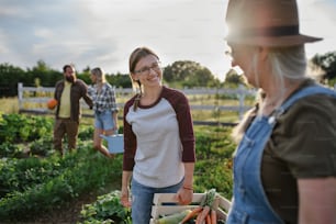 Happy mid adult female farmer hugging her senior peer holding basket with homegrown vegetables outdoors at community farm.