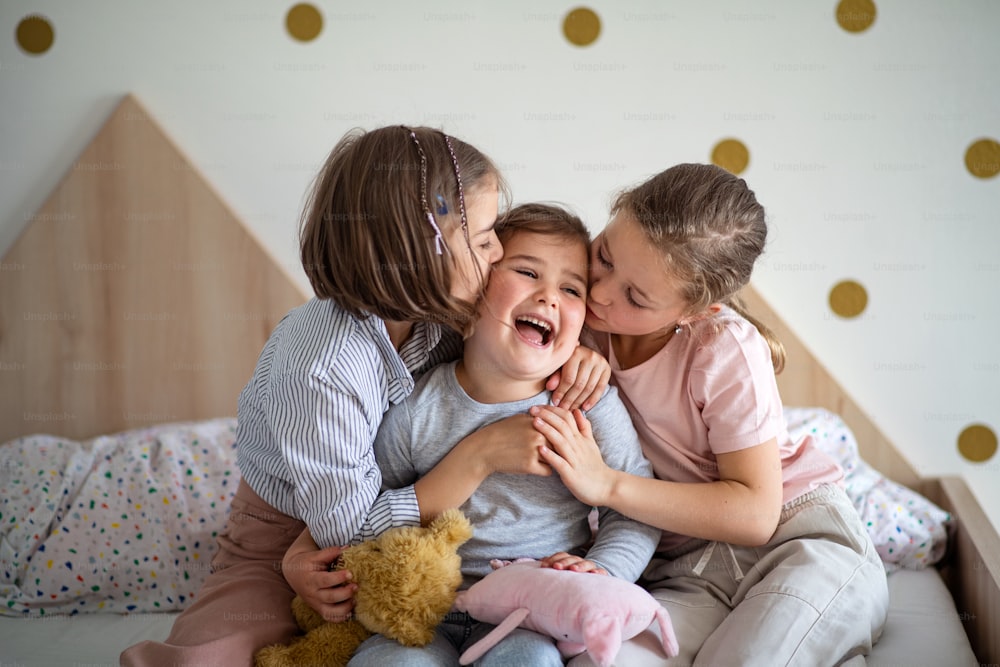 A portrait of three girls sisters indoors at home, kissing.