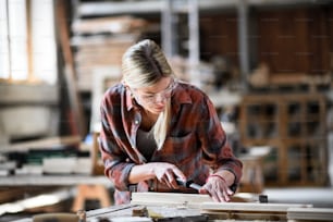 Una carpintera con gafas trabajando en su producto en el interior de un taller de carpintería.