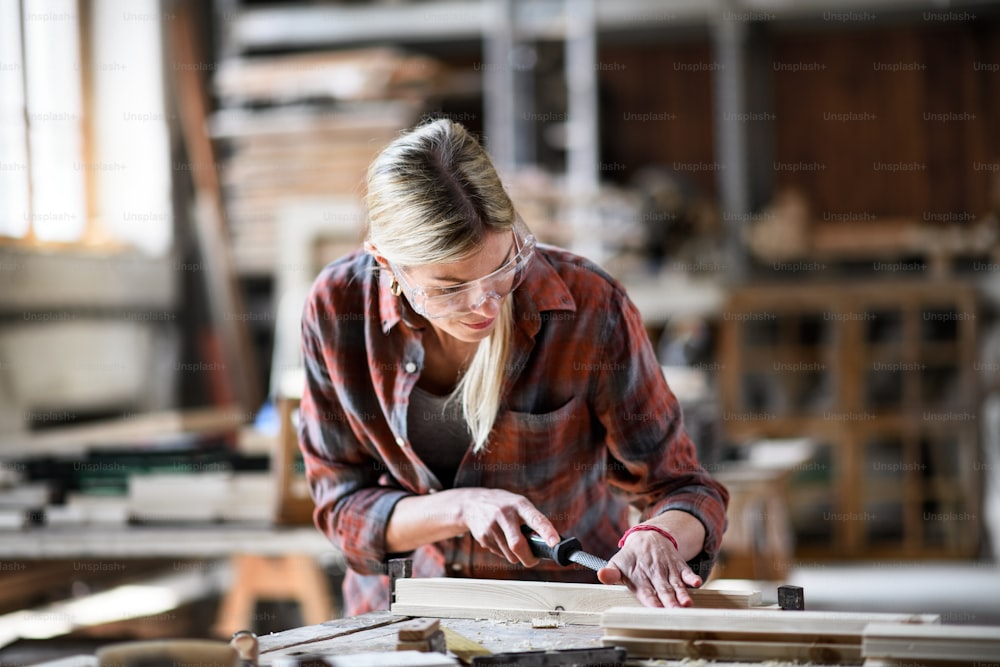 ゴーグルを装着した女性大工が、大工仕事の作業場で屋内で製品に取り組んでいる。