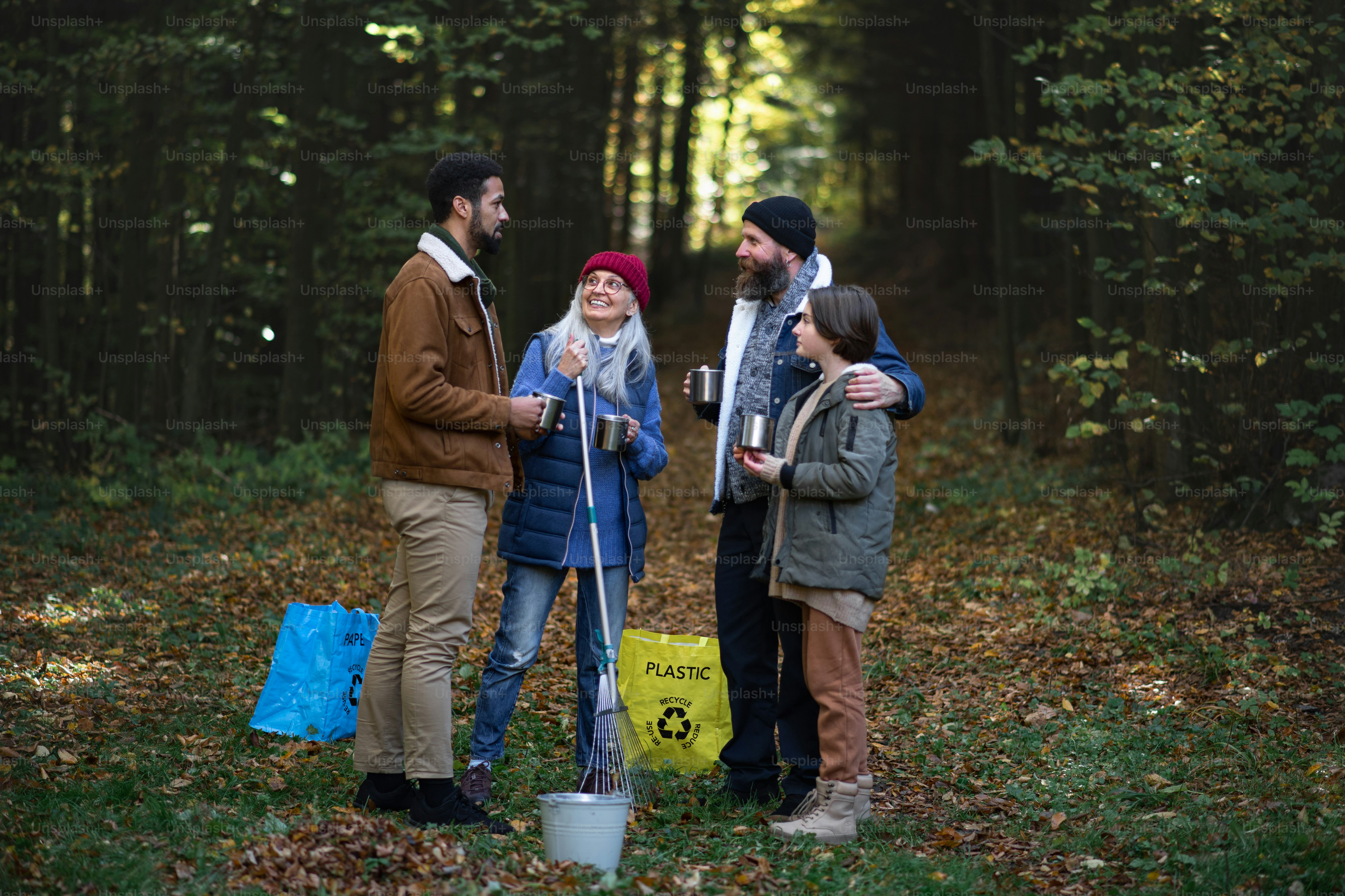 Un grupo diverso de voluntarios felices limpiando el bosque, descansando, bebiendo té y hablando juntos.