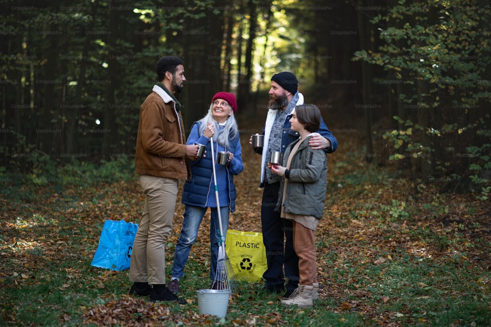 Um grupo diversificado de voluntários felizes limpando a floresta, fazendo pausa, bebendo chá e conversando juntos.