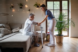 Un travailleur de la santé ou un soignant rend visite à une femme âgée à l’intérieur de son domicile pour l’aider à marcher.