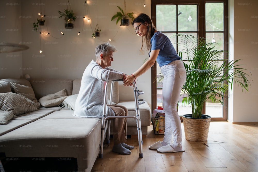A healthcare worker or caregiver visiting senior woman indoors at home, helping her to walk.