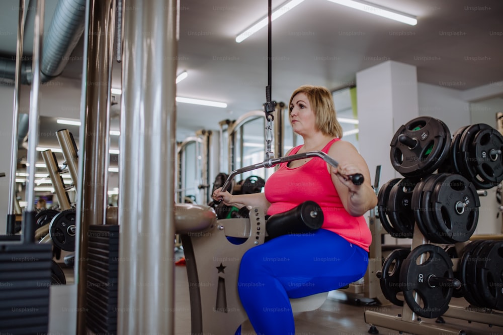 A mid adult plus size woman working out on a lat pulldown machine indoors in gym