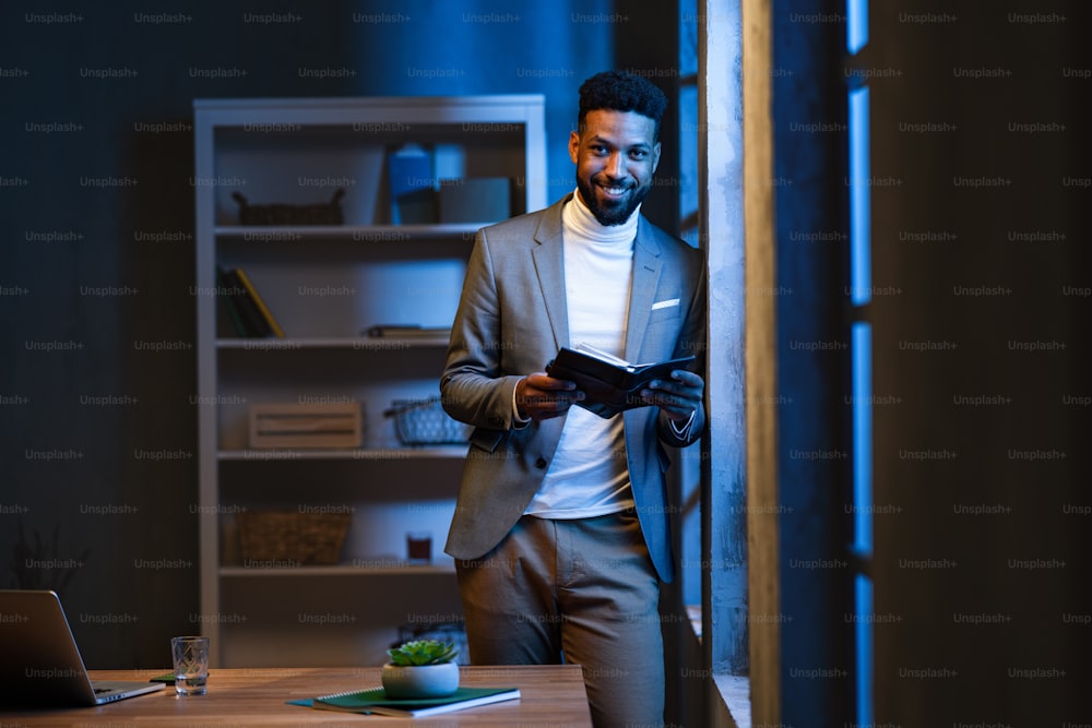 Young african american businessman with diary indoors in an office at night, looking at camera.