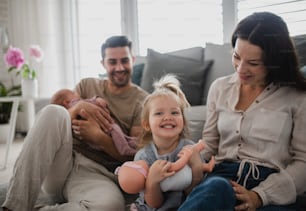 Eine glückliche junge Familie mit neugeborenem Baby und kleinem Mädchen, die die gemeinsame Zeit zu Hause genießen.