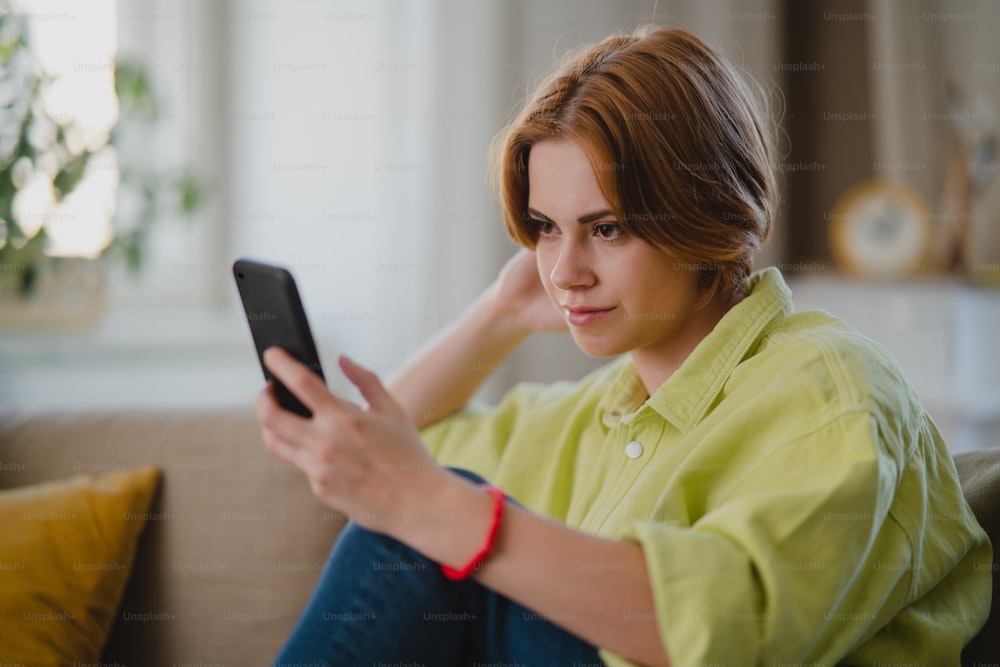 Un retrato de una mujer joven usando un teléfono inteligente tomando selfie, en el interior de la casa, concepto de redes sociales.