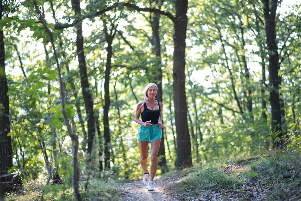 A happy active senior woman jogging outdoors in forest.
