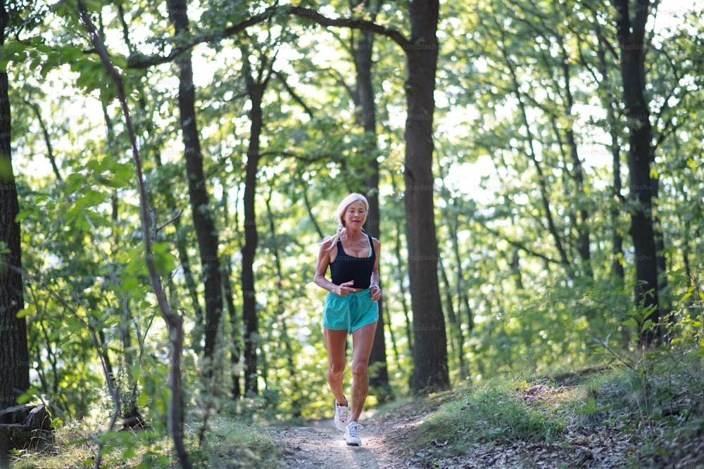 Eine fröhliche aktive Seniorin joggt draußen im Wald.