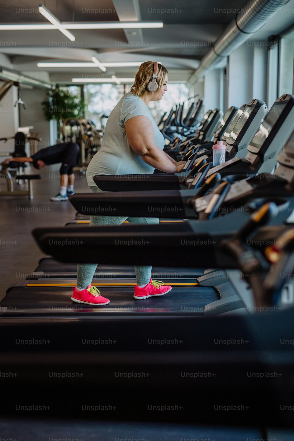 Mid adult overweight woman with headphones running on treadmill in gym