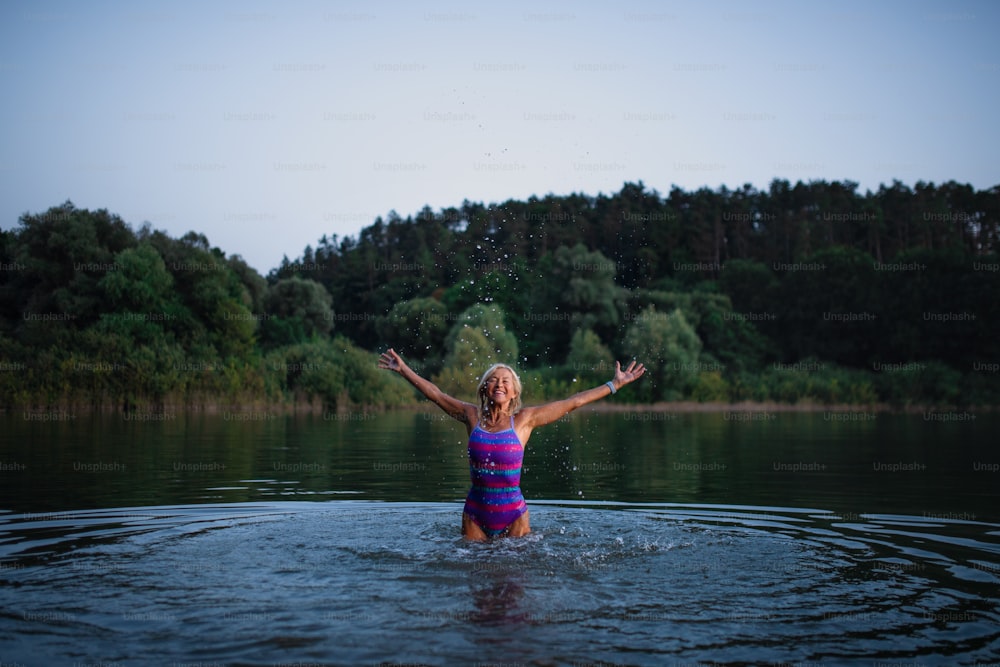 Une nageuse senior active et heureuse éclaboussant de l’eau à l’extérieur dans un lac.