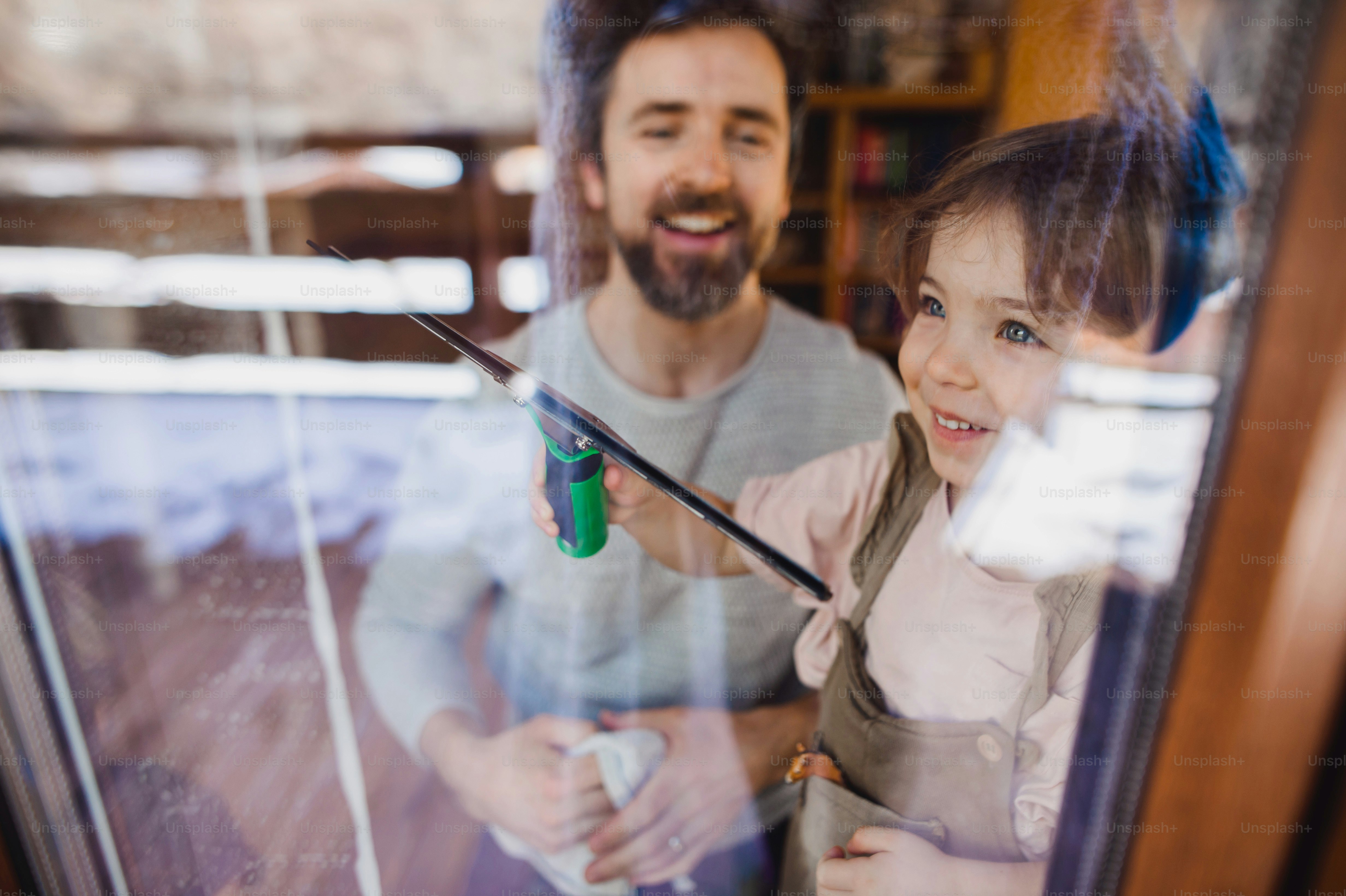 A happy girl with father cleaning windows at home, daily chores concept ...