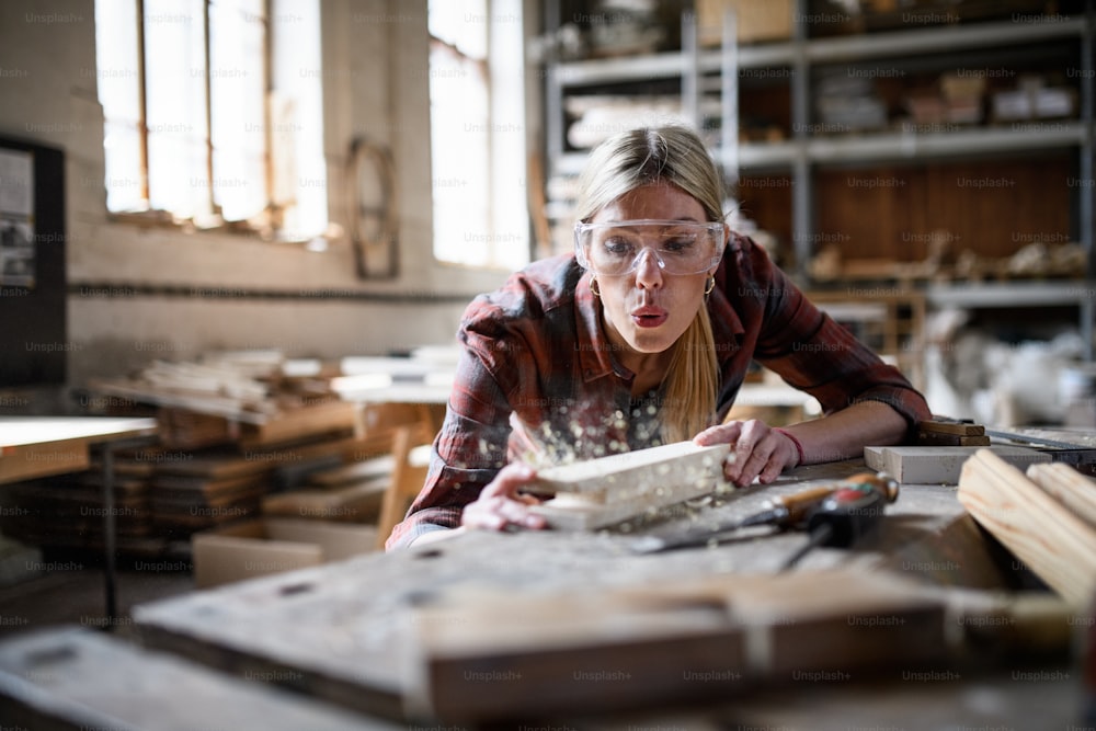 ゴーグルを装着した女性大工が、大工仕事の作業場で屋内で製品に取り組んでいる。