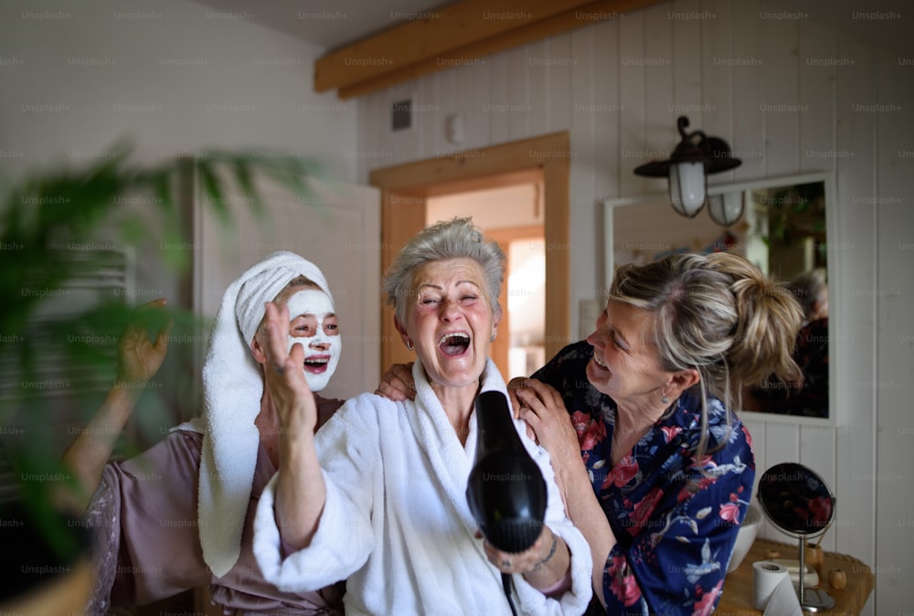 Happy senior women friends in bathrobes having fun indoors at home, a selfcare concept.