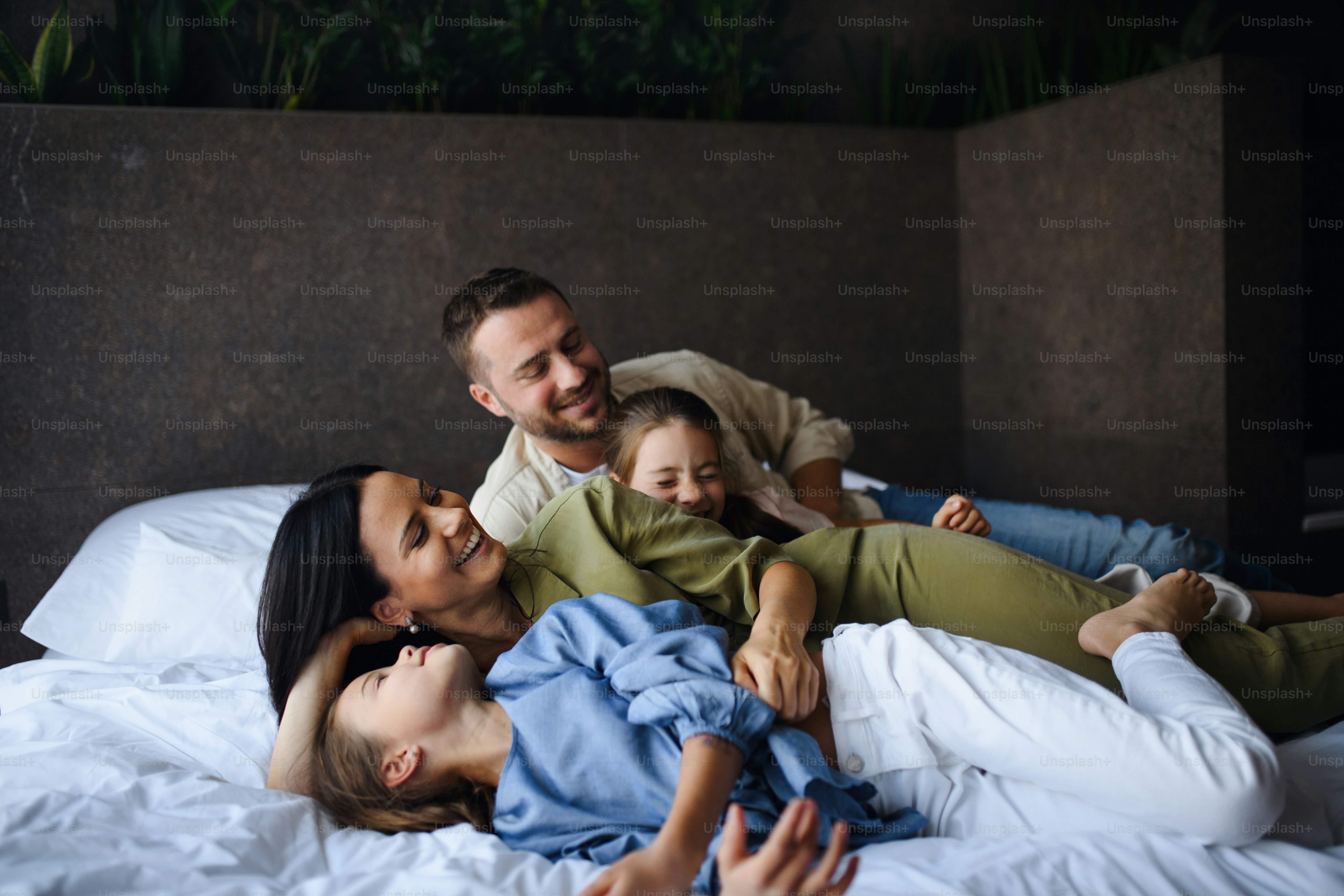 Una familia joven feliz con dos niños acostados en la cama en el hotel ...