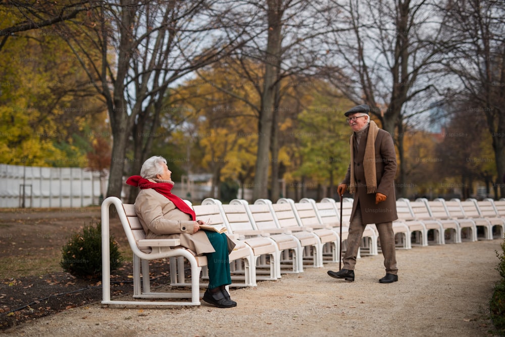 A happy senior couple meeting outdoors in park on autumn day.