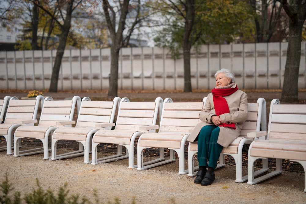 A senior woman sitting on bench in town park in autumn, resting