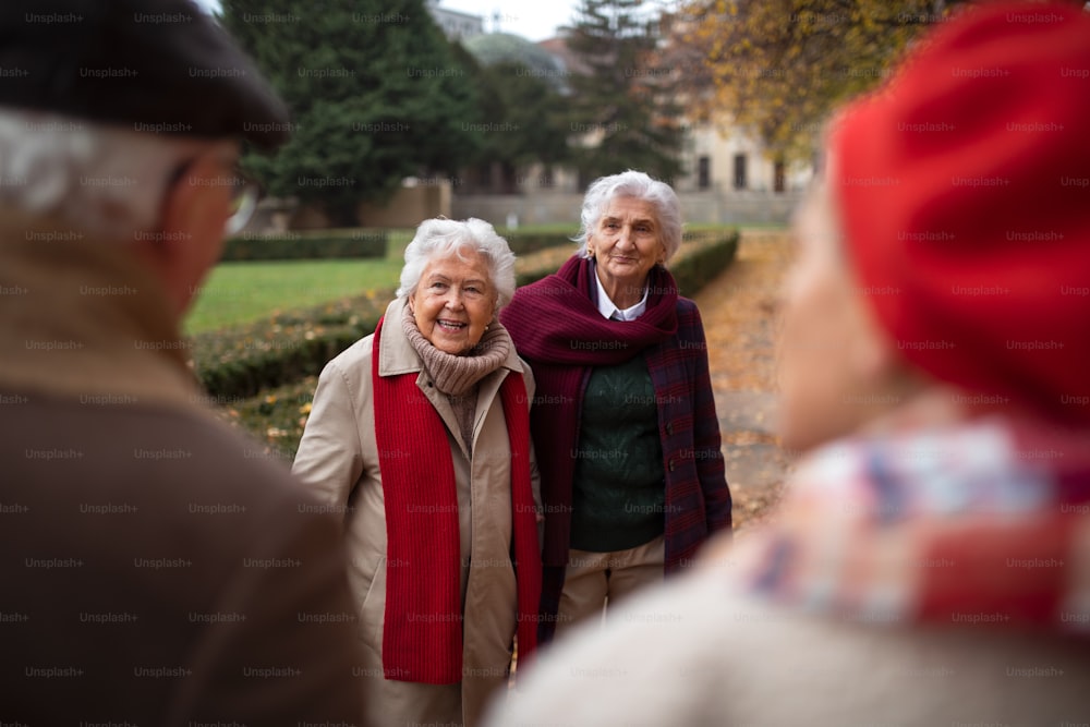 A group of happy senior friends on walk outdoors in town park in autumn, talking and laughing.