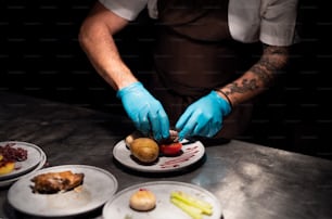 Mains de chef dans des gants servant et décorant son repas dans la cuisine du restaurant
