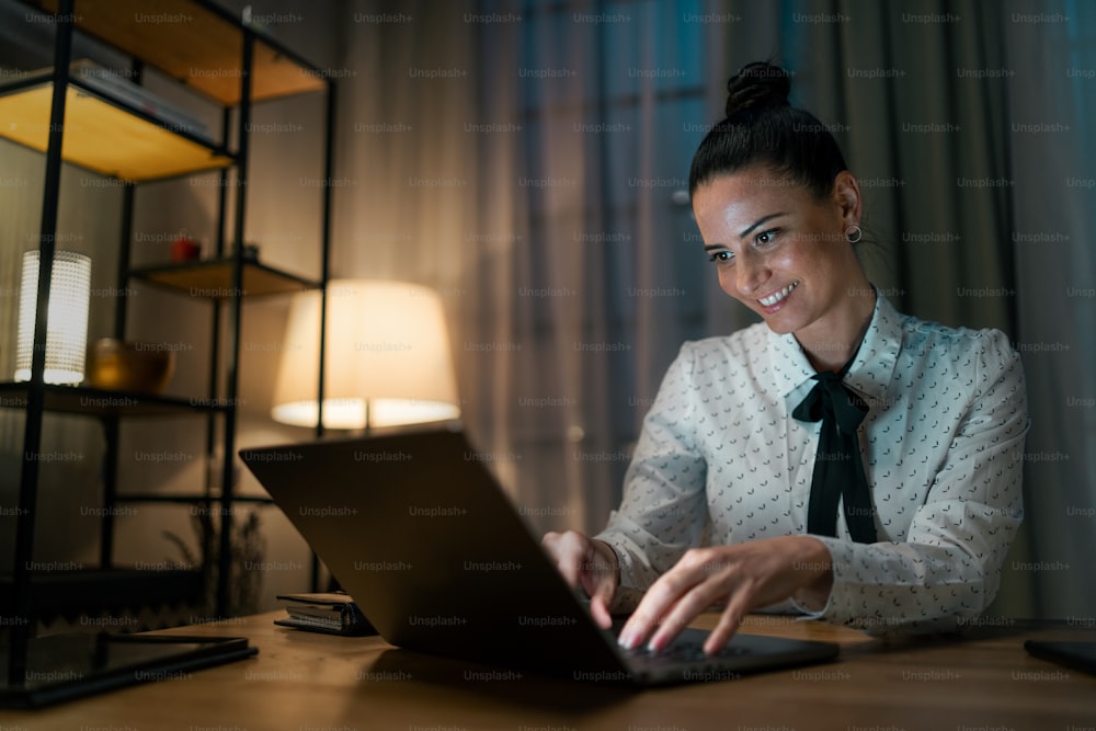 A happy mid adult business woman working on laptop in office at night.