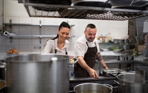 Un chef et un cuisinier heureux qui travaillent sur leurs plats à l’intérieur dans la cuisine d’un restaurant.