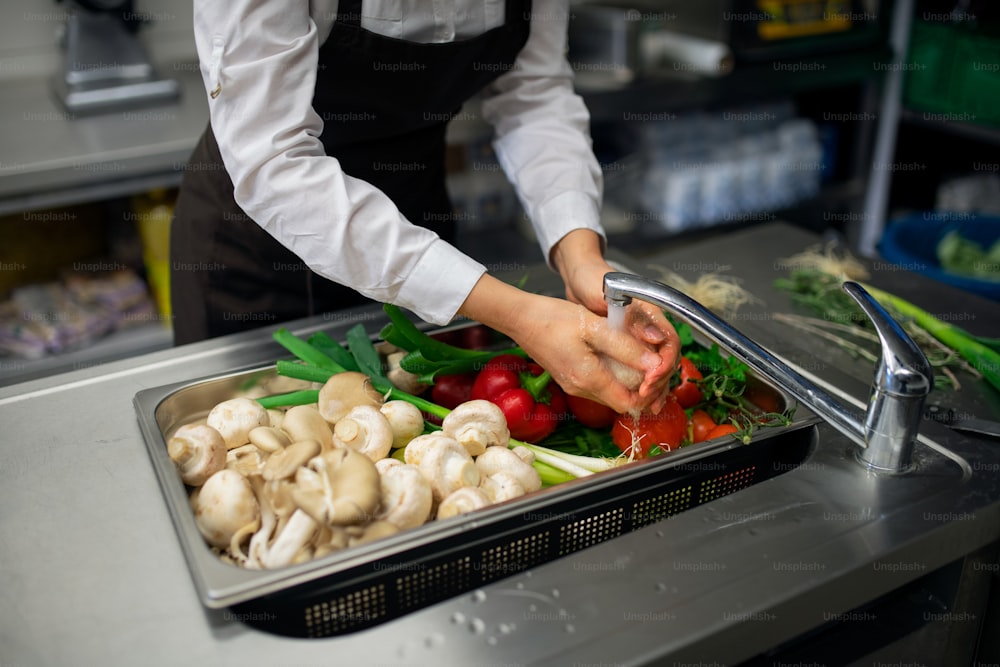 A close-up of cook washing vegetables in sink in commercial kitchen.