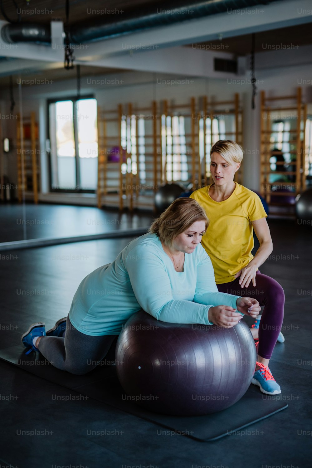 Una mujer con sobrepeso haciendo ejercicio con un entrenador personal en la pelota fintess en el gimnasio