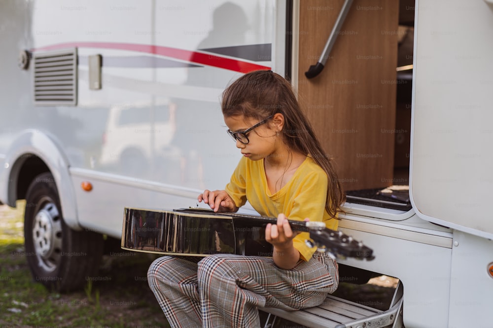 Menina pequena feliz com guitarra tocando por caravana, viagem de férias em família.