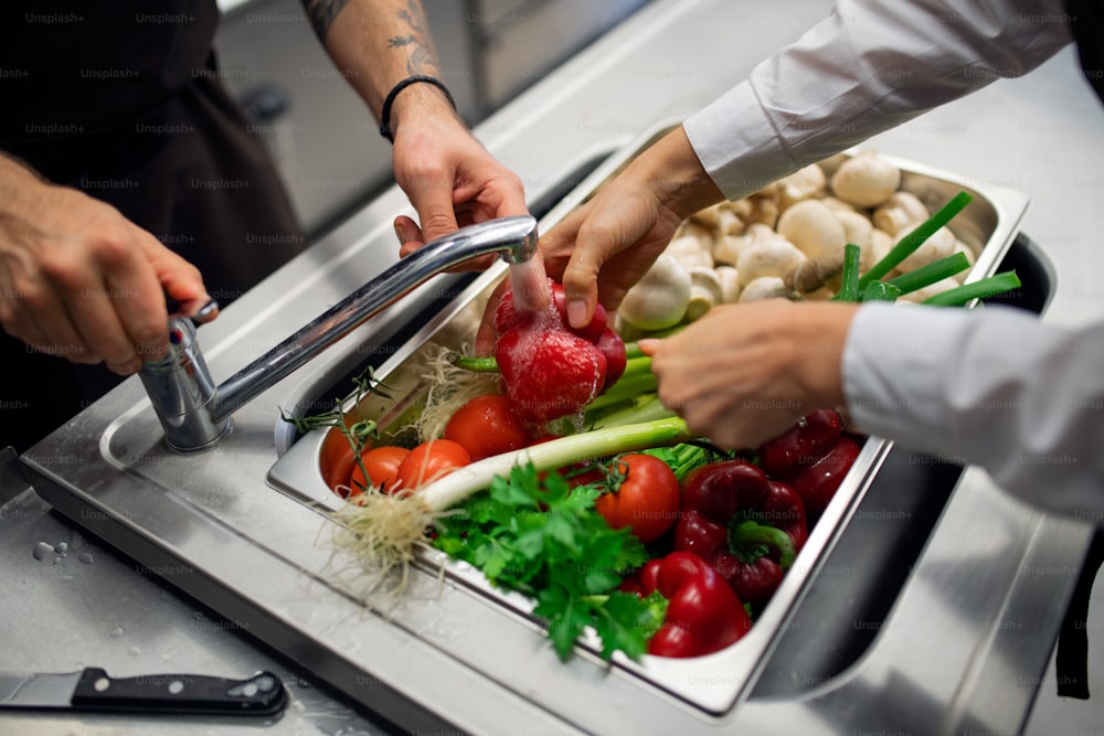 A close-up of cook washing vegetables in sink in commercial kitchen.