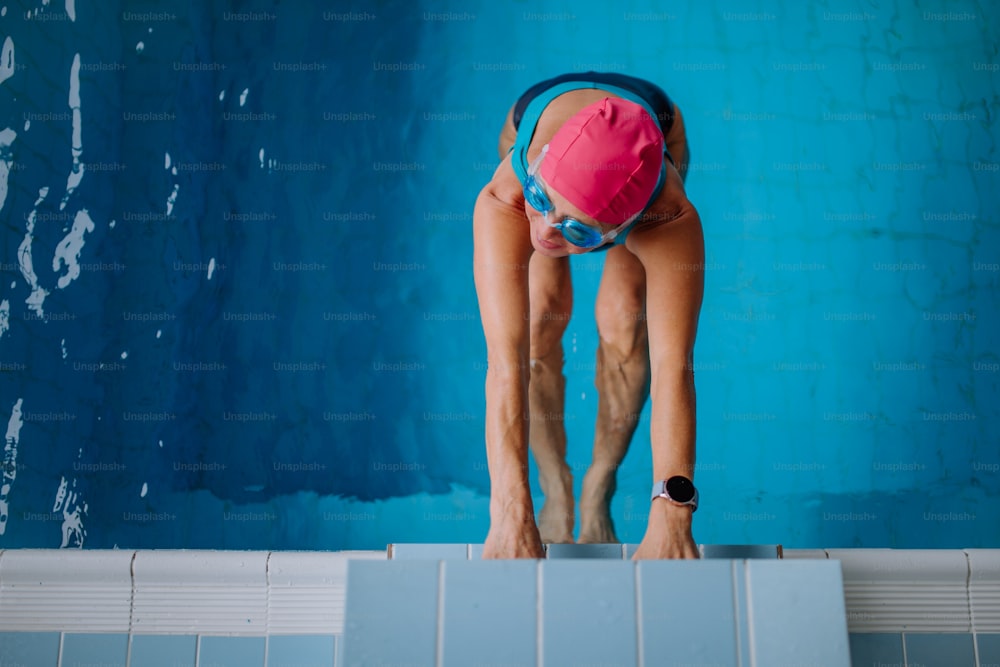 Uma vista superior da nadadora sênior ativa segurando o bloco de partida na piscina coberta.