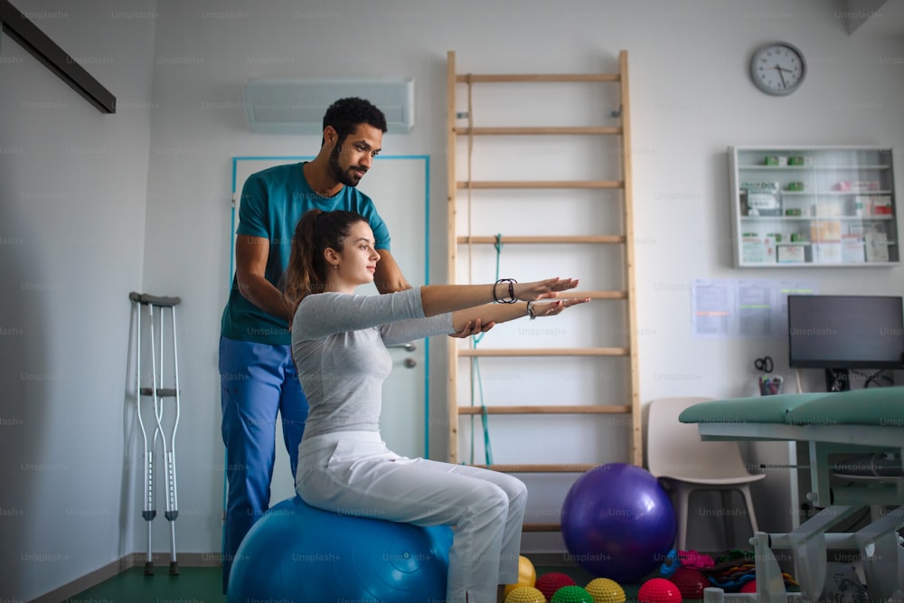 A young male physiotherapist exercising with young woman patient in a physic room