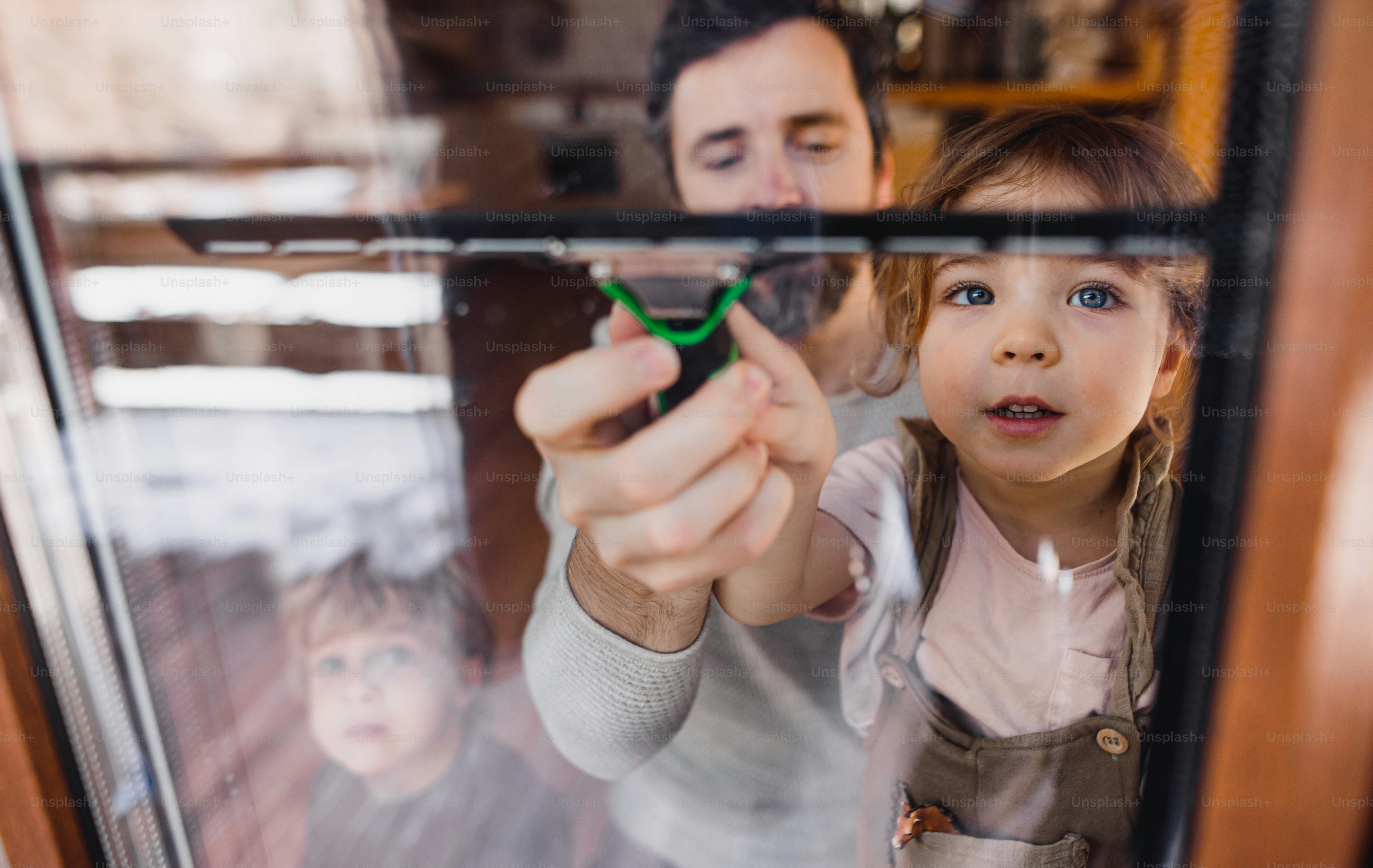 A happy girl with father cleaning windows at home, daily chores concept ...