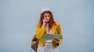 A young woman tourist outdoors against white background on trip in town, using paper map.