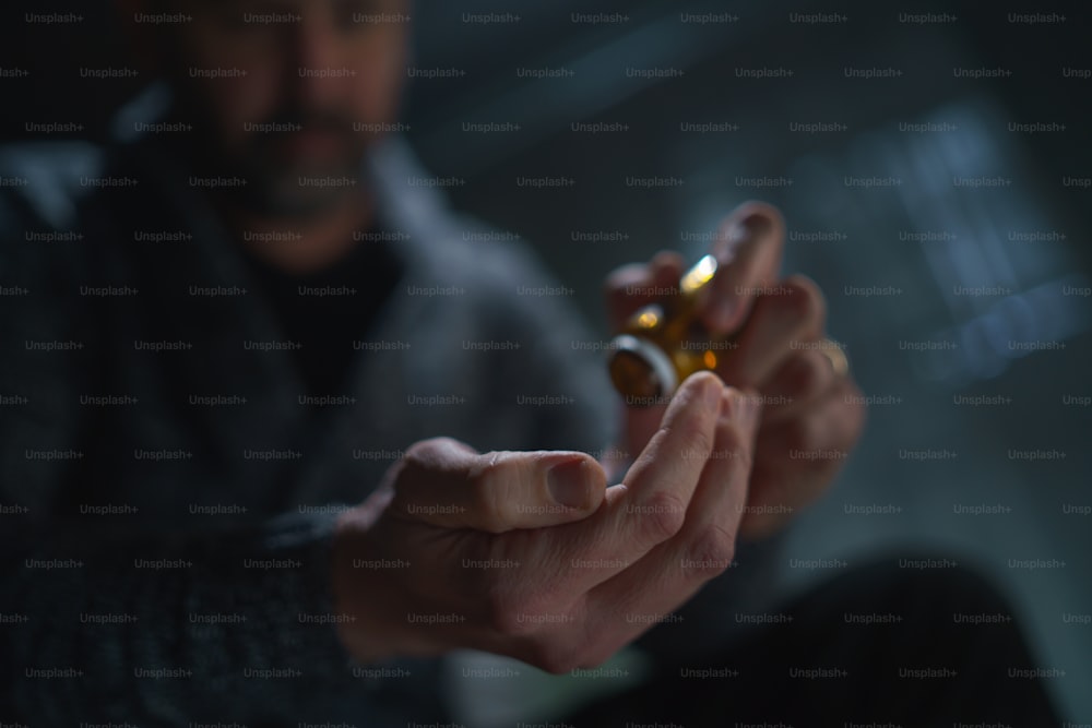 A blurred man holding and show drug pill on dark background, mental health concept.