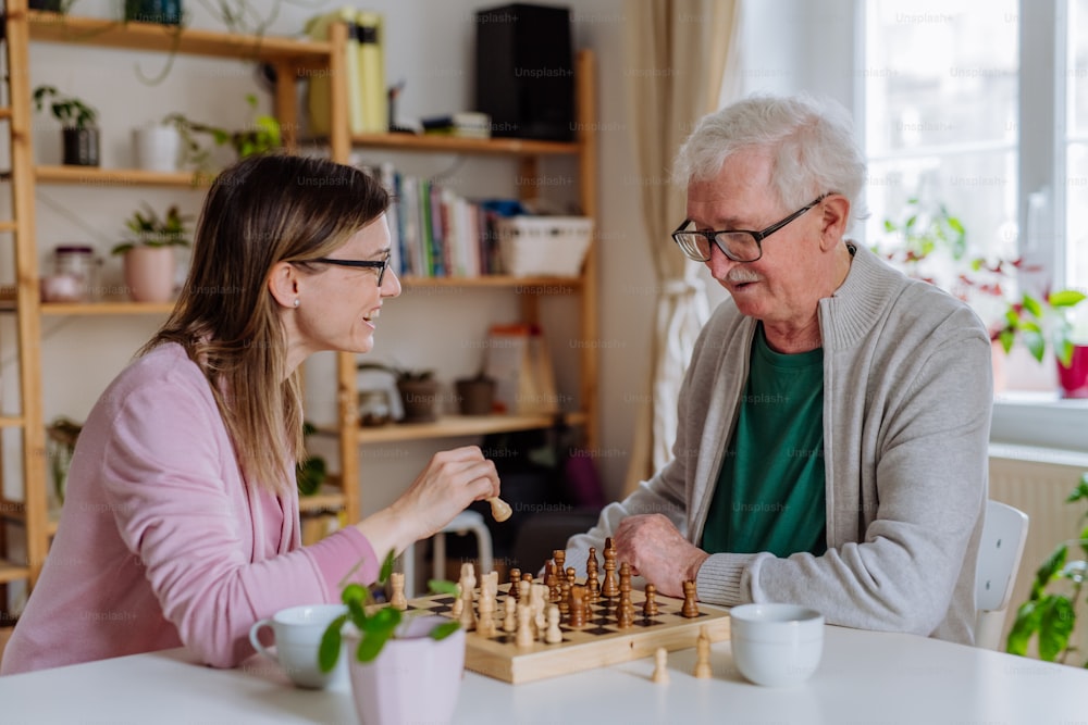 Une fille adulte rend visite à son père aîné à la maison et joue aux échecs ensemble.
