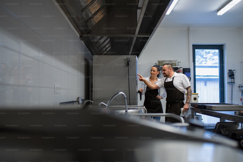 A chef teaching cook how to use combi oven indoors in restaurant kitchen.