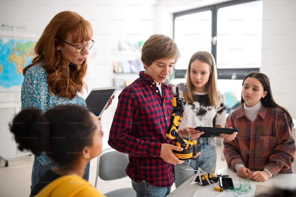 College student presenting his builded robotic toy to a young science teacher and his schoolmates at robotics classroom at school.