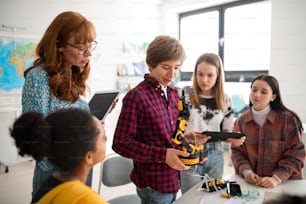 College student presenting his builded robotic toy to a young science teacher and his schoolmates at robotics classroom at school.