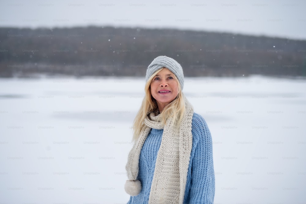 Front view portrait of happy senior woman outdoors standing in snowy nature.