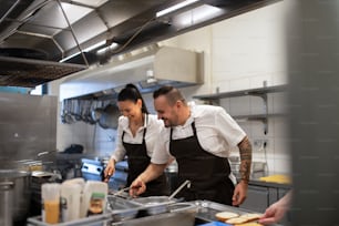 Un chef et un cuisinier heureux qui travaillent sur leurs plats à l’intérieur dans la cuisine d’un restaurant.